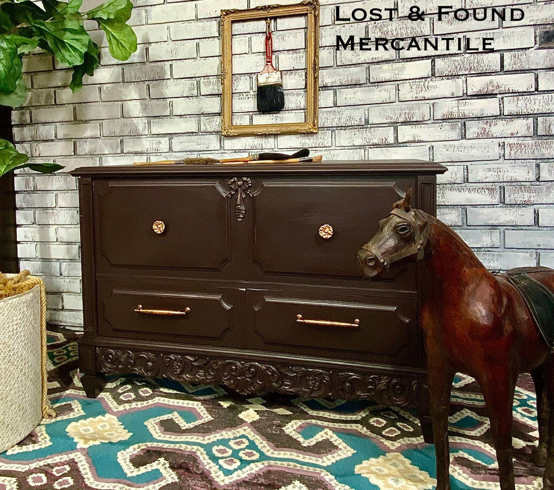 Dark wooden dresser with gold handles against a brick wall, with a horse model in front.