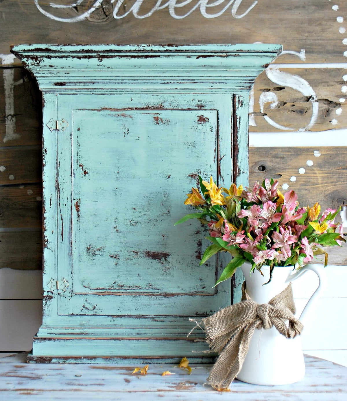 Vintage turquoise cabinet with a white pitcher of flowers on a wooden background