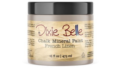 A jar of Dixie Belle Chalk Mineral Paint in the color French Linen, featuring a black lid and a beige label with red and blue lettering.