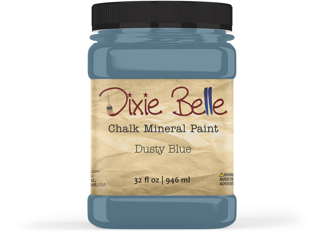 A jar of Dixie Belle Chalk Mineral Paint in the color 'Dusty Blue', featuring a black lid and a beige textured label, shown on a white background.