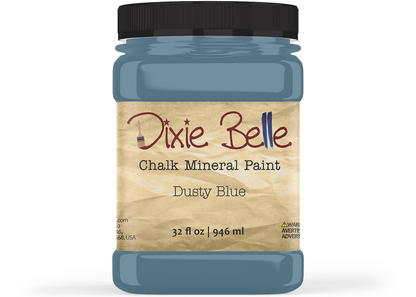 A jar of Dixie Belle Chalk Mineral Paint in the color 'Dusty Blue', featuring a black lid and a beige textured label, shown on a white background.