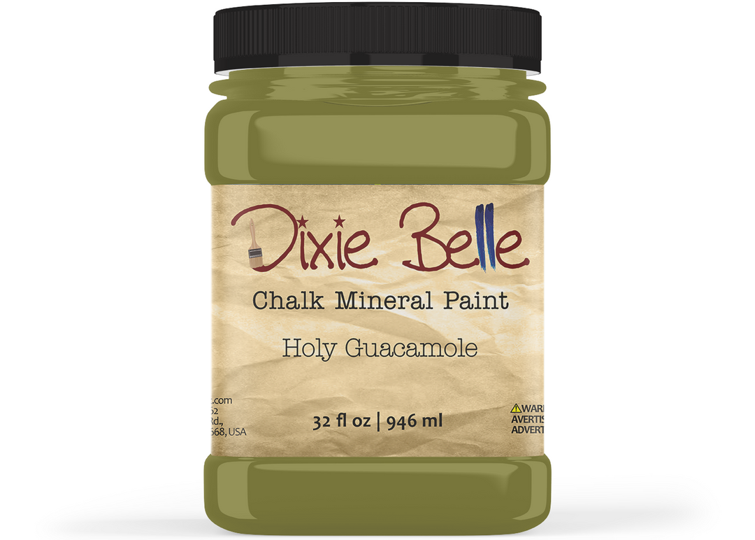 A jar of Dixie Belle Chalk Mineral Paint in the color Holy Guacamole, featuring an olive green paint visible through the clear container and a beige label with the brand name in red script.