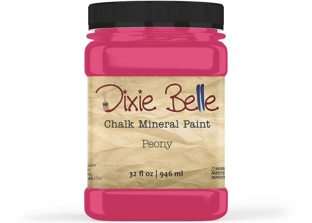 A jar of Dixie Belle Chalk Mineral Paint in the shade Peony, featuring a bright pink paint jar with a black lid and a beige textured label.