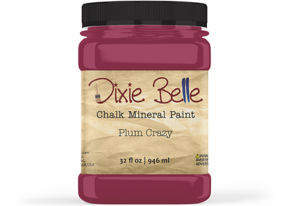 A jar of Dixie Belle Chalk Mineral Paint in the shade Plum Crazy, featuring a black lid and a beige textured label, shown on a white background.