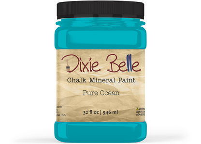 A jar of Dixie Belle Chalk Mineral Paint in the color 'Pure Ocean', featuring a bright turquoise blue paint visible through the clear jar, a black lid, and a beige label with brown and black text.