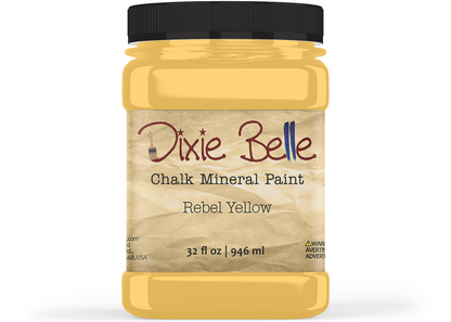 A jar of Dixie Belle Chalk Mineral Paint in the shade Rebel Yellow, featuring a black lid and a beige textured label, set against a plain white background.