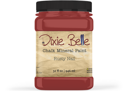 A jar of Dixie Belle Chalk Mineral Paint in the color 'Rusty Nail', featuring a black lid and a beige textured label, shown on a white background.