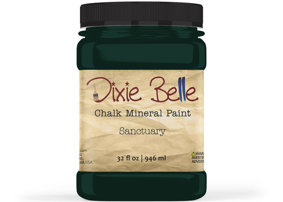 A jar of Dixie Belle Chalk Mineral Paint in the color 'Sanctuary', featuring a dark forest green paint jar with a black lid and a beige textured paper label.