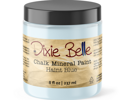 A jar of Dixie Belle Chalk Mineral Paint in the color Haint Blue, featuring a light blue container, a black lid, and a brown paper-textured label.