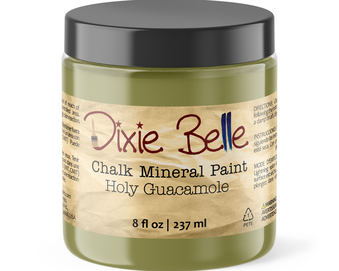 A jar of Dixie Belle Chalk Mineral Paint in the color Holy Guacamole, featuring an olive green container, a black lid, and a beige label with red and blue lettering.