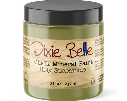 A jar of Dixie Belle Chalk Mineral Paint in the color Holy Guacamole, featuring an olive green container, a black lid, and a beige label with red and blue lettering.