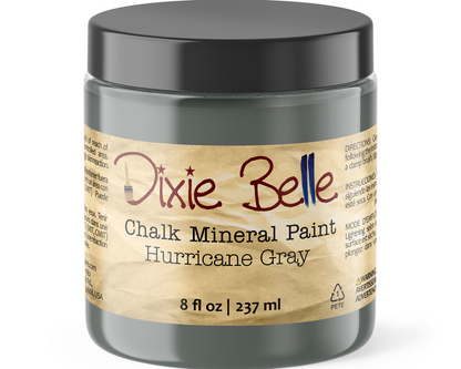 A jar of Dixie Belle Chalk Mineral Paint in the color Hurricane Gray, featuring a dark gray container and a beige label with red and blue lettering.