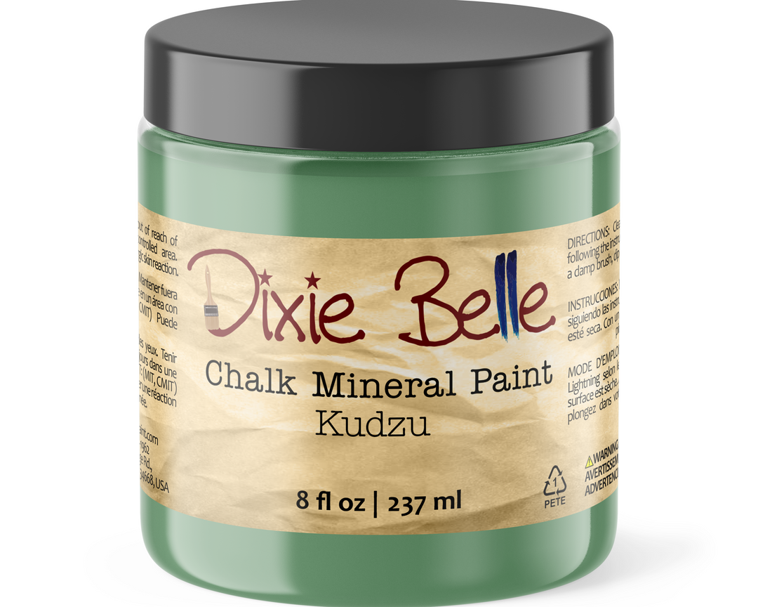 A jar of Dixie Belle Chalk Mineral Paint in the color Kudzu, featuring a translucent green container, a black lid, and a textured beige paper label.