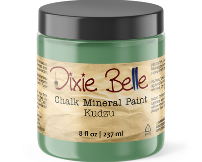 A jar of Dixie Belle Chalk Mineral Paint in the color Kudzu, featuring a translucent green container, a black lid, and a textured beige paper label.