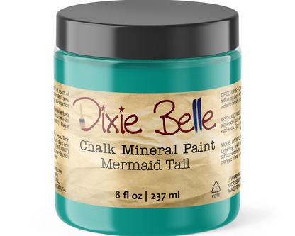 A jar of Dixie Belle Chalk Mineral Paint in the Mermaid Tail color, featuring a teal-green container, a black lid, and a beige paper label with red and black text.