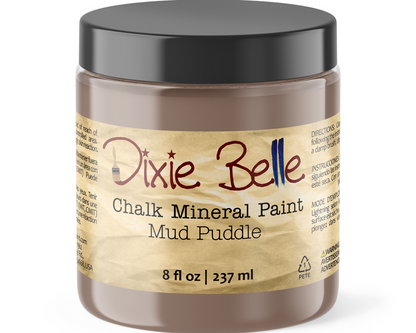 A jar of Dixie Belle Chalk Mineral Paint in the Mud Puddle shade, featuring a black lid and a beige label with brown and red text.