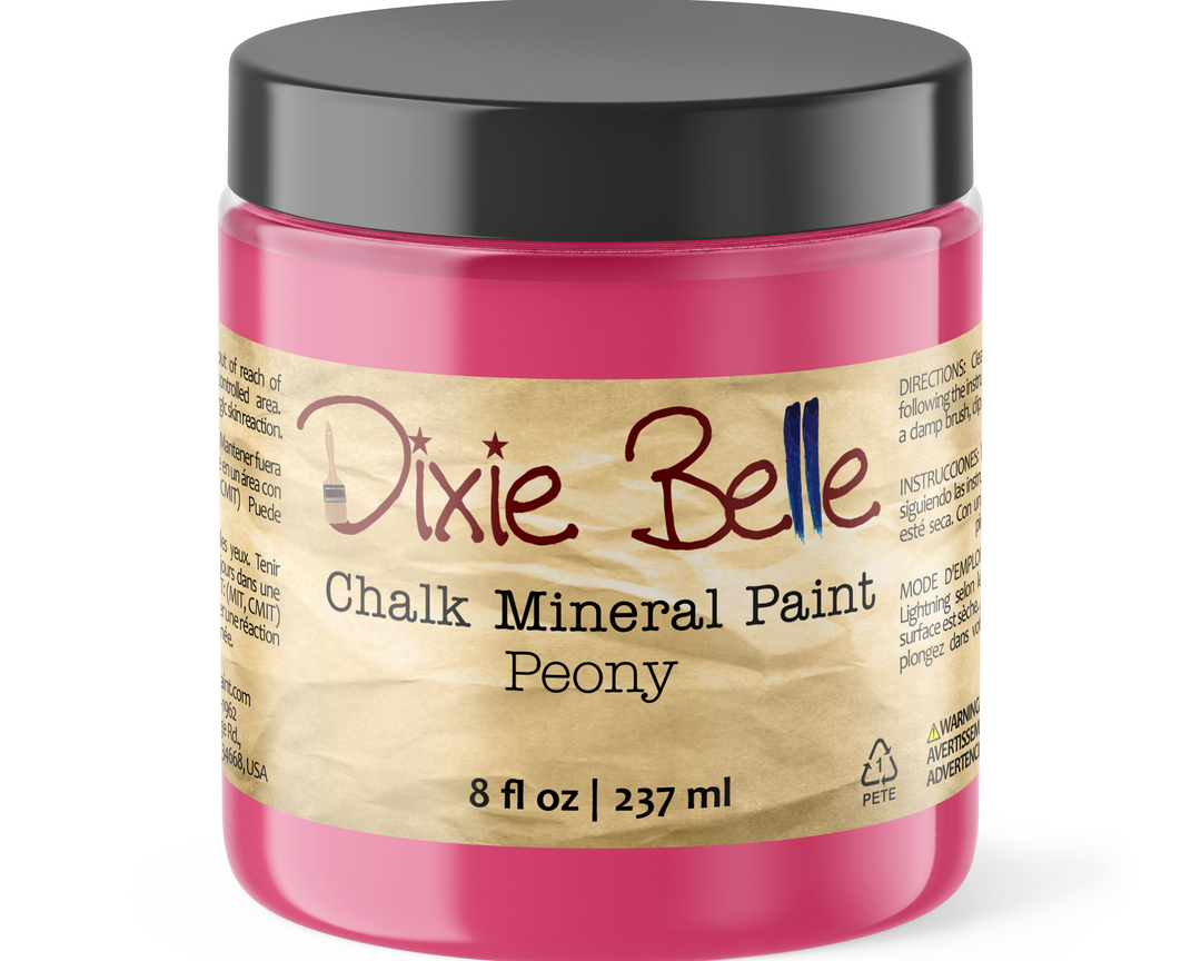 A jar of Dixie Belle Chalk Mineral Paint in the color Peony, featuring a bright pink paint inside, a black lid, and a beige label with the brand name in red and blue script.