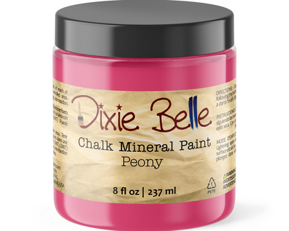 A jar of Dixie Belle Chalk Mineral Paint in the color Peony, featuring a bright pink paint inside, a black lid, and a beige label with the brand name in red and blue script.