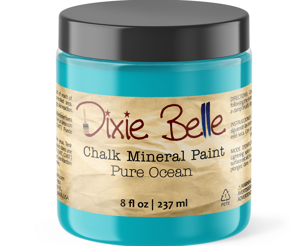A jar of Dixie Belle Chalk Mineral Paint in the color 'Pure Ocean', featuring a bright turquoise blue paint inside, a black screw-on lid, and a beige paper label with red and blue lettering.