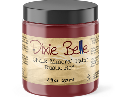 A jar of Dixie Belle Chalk Mineral Paint in the color Rustic Red, featuring a black lid and a beige label with red and black text.