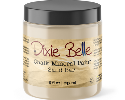 A jar of Dixie Belle Chalk Mineral Paint Sand Bar, 8 fl oz, containing a light beige paint, with a black lid and a textured tan label.
