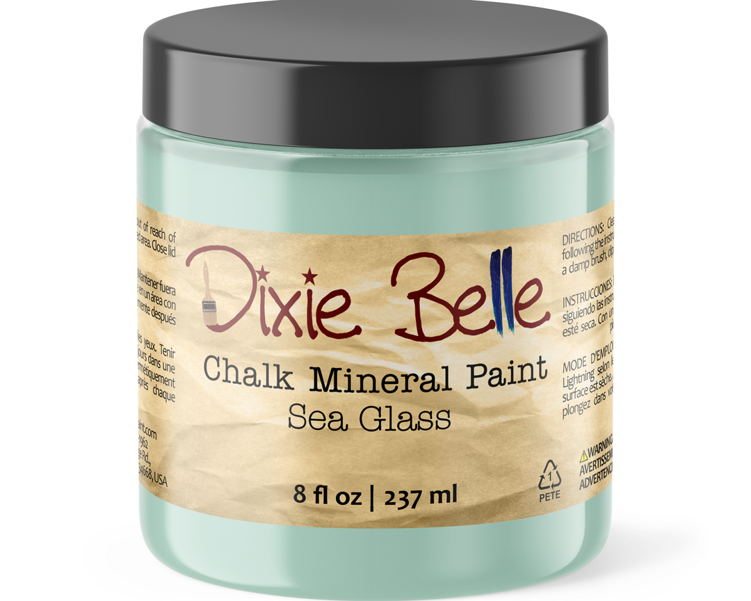 A jar of Dixie Belle Chalk Mineral Paint in the color Sea Glass, featuring a light teal-green paint visible through the clear container, a black lid, and a beige paper label.