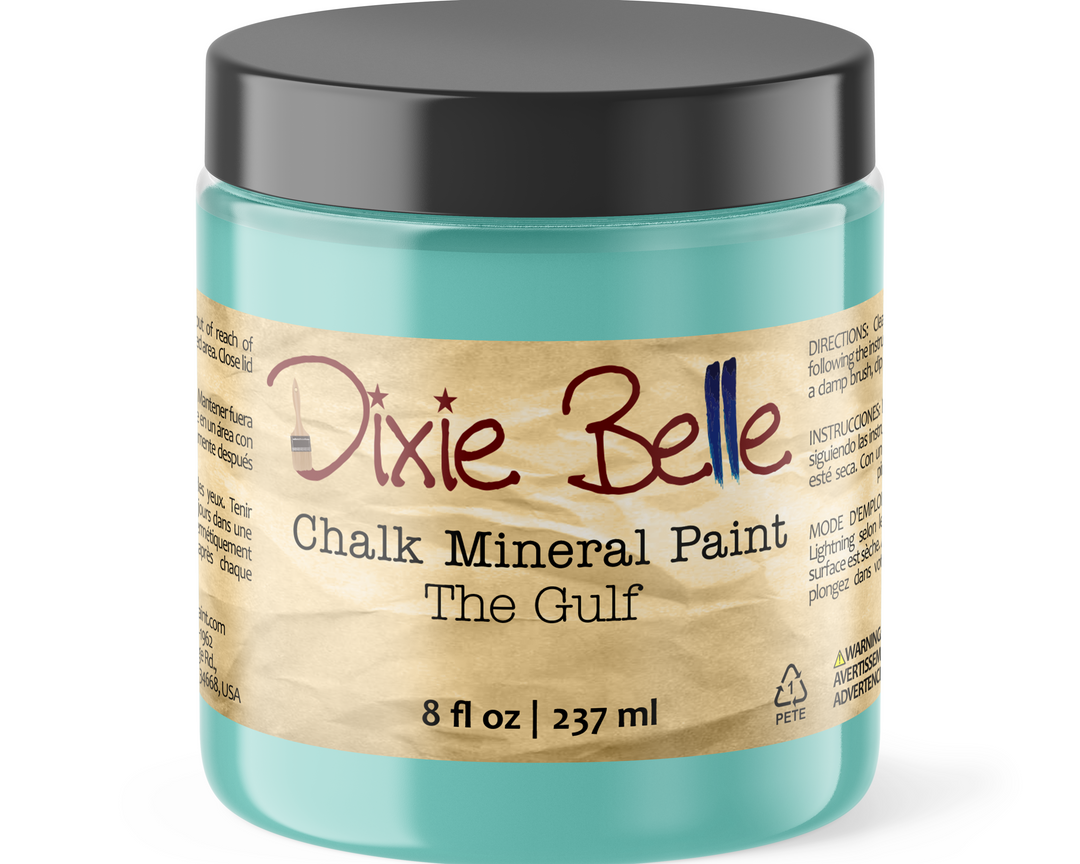 A jar of Dixie Belle Chalk Mineral Paint in the shade 'The Gulf', featuring a translucent aqua blue container, a black lid, and a beige paper label.