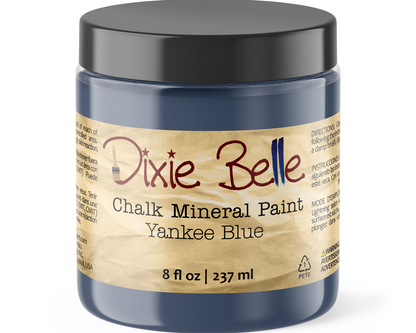 A jar of Dixie Belle Chalk Mineral Paint in the color Yankee Blue, featuring a black lid and a beige label with red and black text.