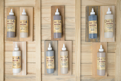 Six squeeze bottles of VooDoo Gel Stain wood finish in various colors, arranged neatly on a light wood plank background.