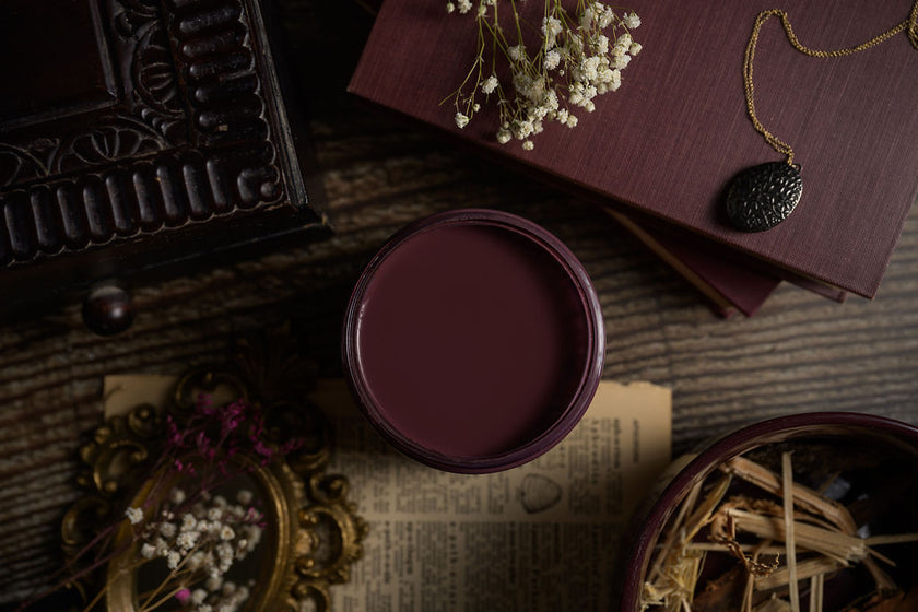 Mauve container on a textured surface with dried flowers and a book