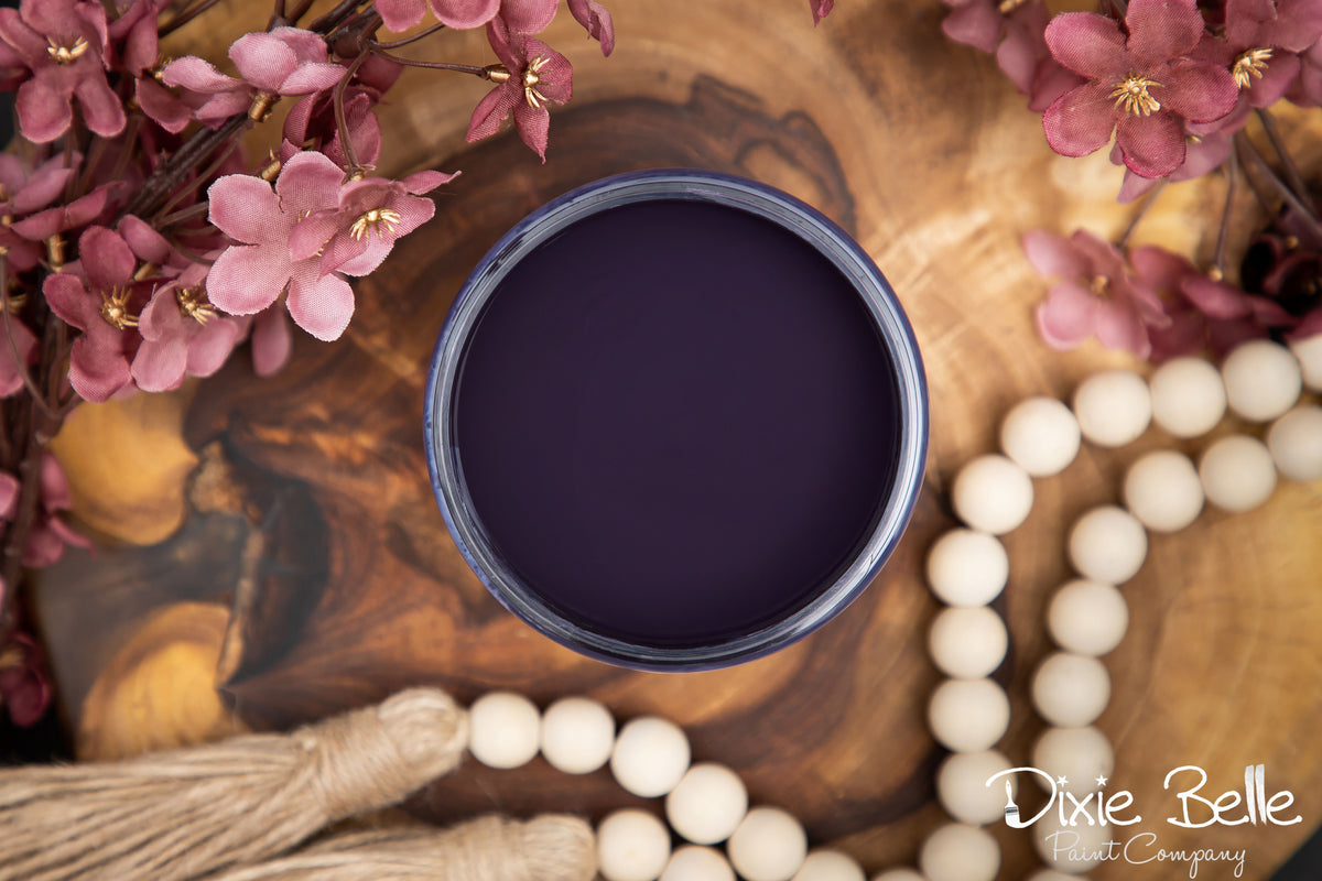 Dark purple bowl on a wooden surface with pink flowers and white beads