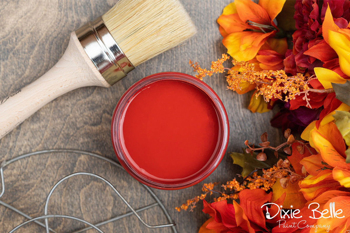 Jar of red paint labeled 'Barn Red' with a paintbrush and autumn-themed decor on a wooden surface.