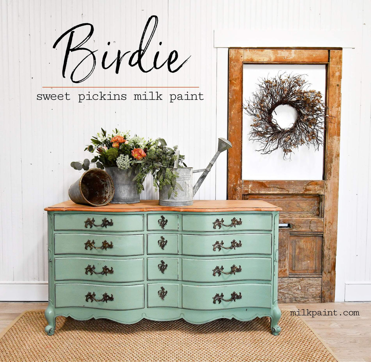 A painted vintage-style chest of drawers in a soft mint green with a natural wood top, styled in a rustic room setting with a wooden door, wreath, and metal watering can on a woven rug. Text on the image reads 'Birdie sweet pickins milk paint'.
