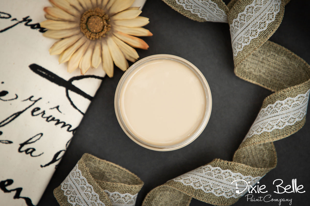 Jar of cream paint on a dark surface with a decorative flower and ribbon
