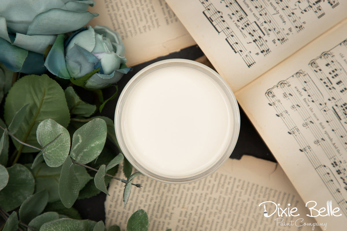 Jar of cream paint on an open book with greenery and music sheet