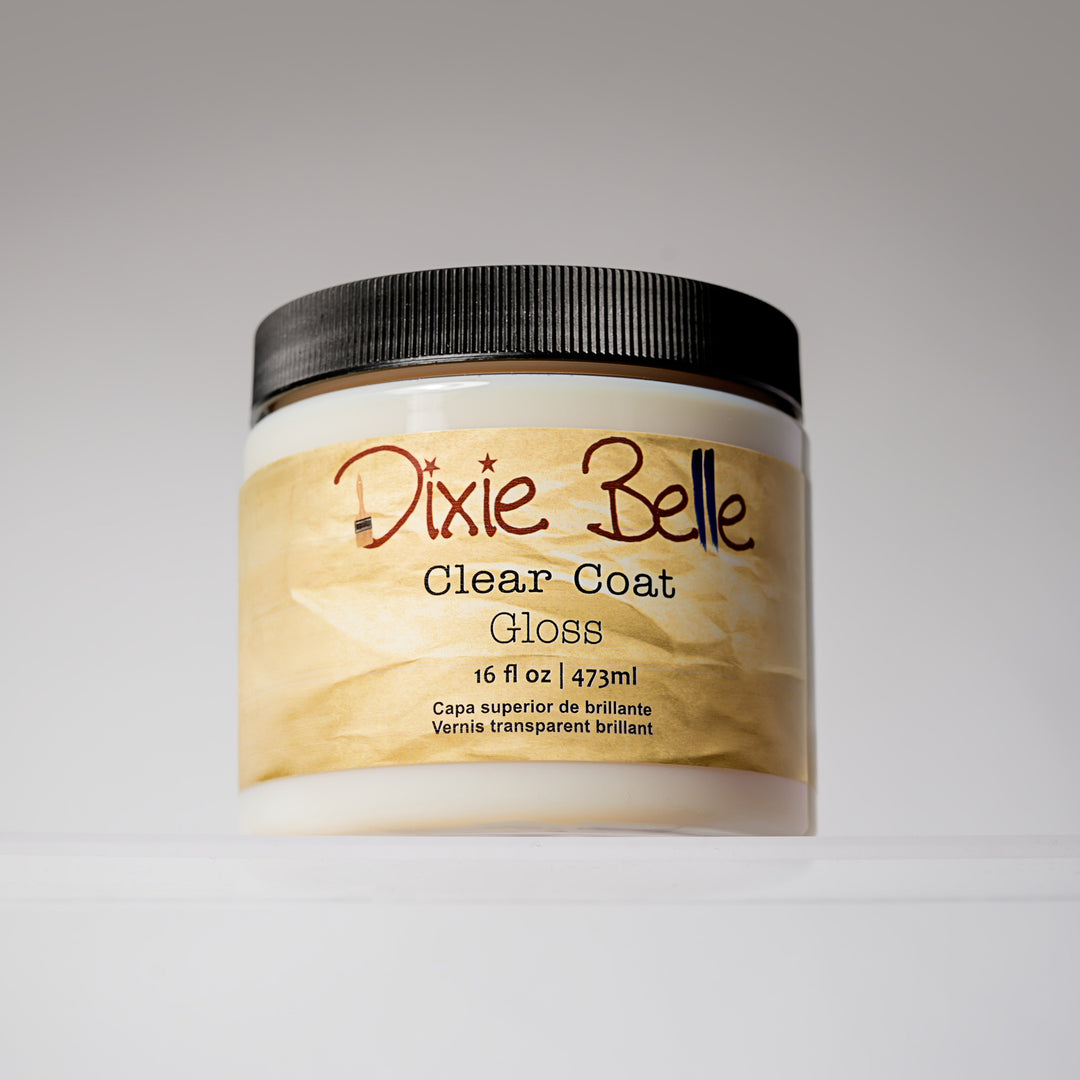 A jar of Dixie Belle Clear Coat Gloss, 16 fl oz, featuring a black ribbed lid and a cream-colored label with a gold marbled pattern.