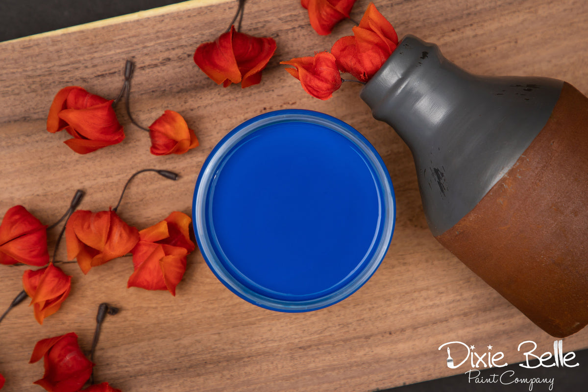 Blue paint can on a wooden surface with red flowers and a bottle.