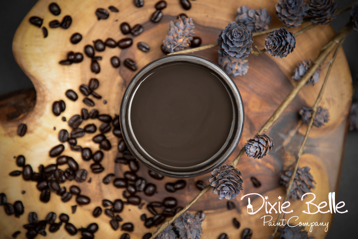 Jar of brown paint on a wooden surface with coffee beans and pine cones, featuring the Dixie Belle Paint Company logo.