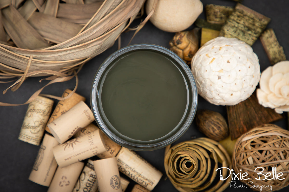 Jar of green paint surrounded by decorative items on a dark surface with 'Dixie Belle' branding.