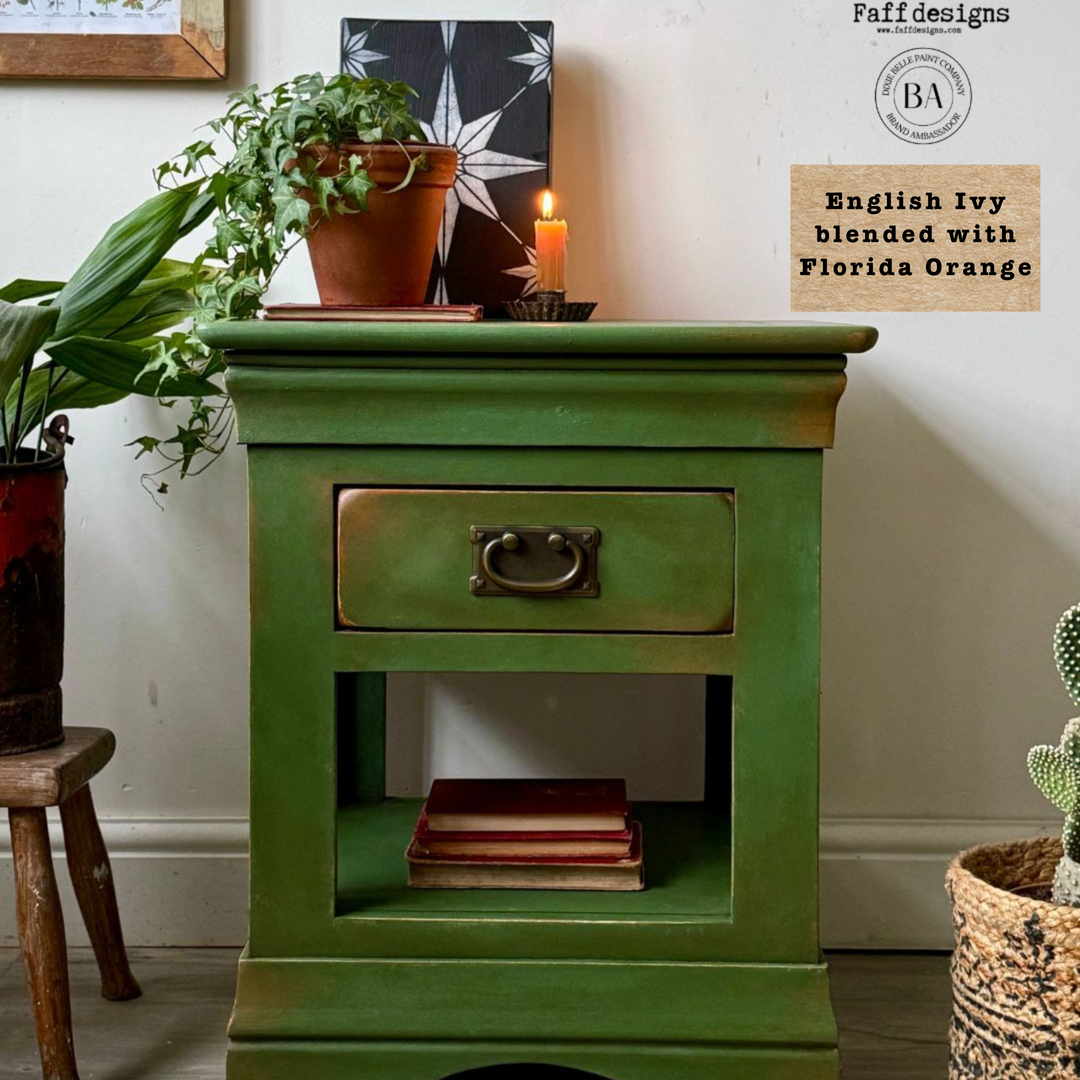 Green wooden side table with a drawer, books, and potted plants in a room setting.