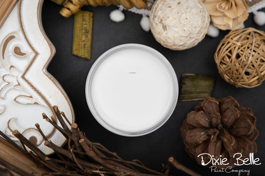Fluff white color paint jar in a decorative container surrounded by natural elements on a dark surface with 'Dixie Belle Paint Company' branding.