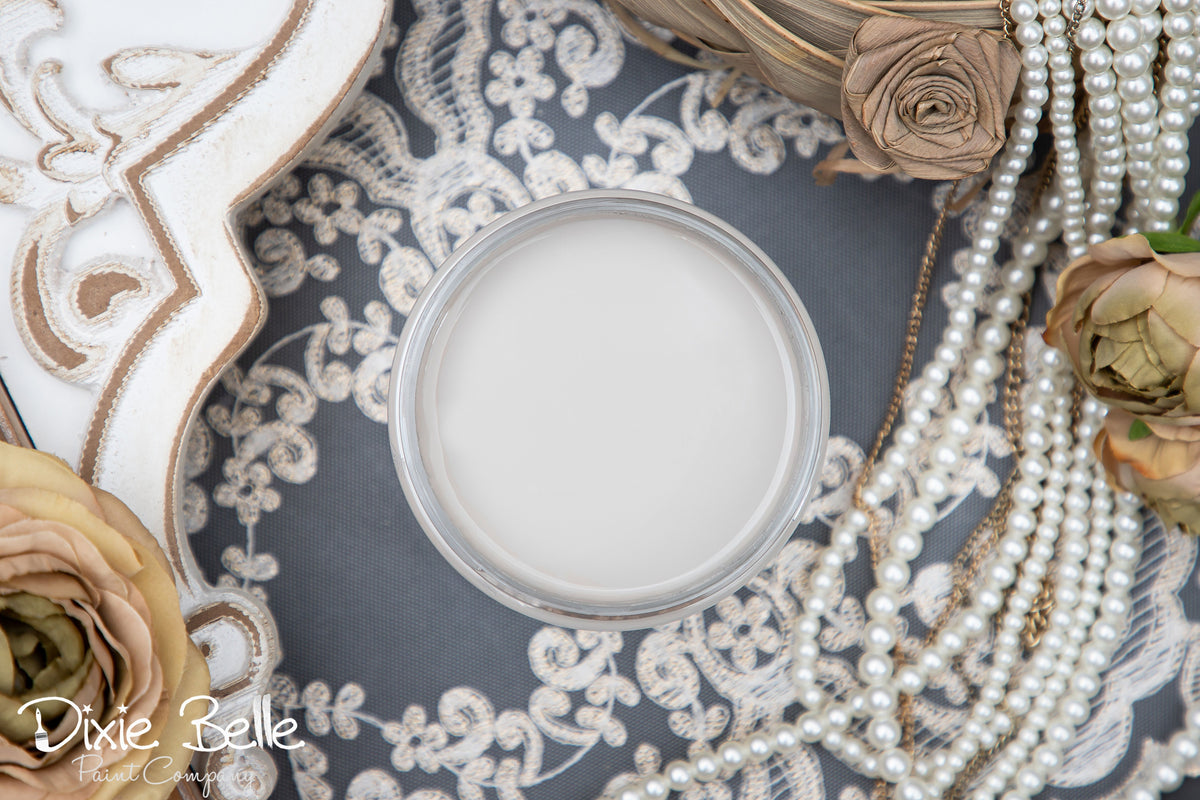 Close-up of a french linen paint jar with pearls and flowers on a textured surface, featuring the brand 'Dixie Belle'.