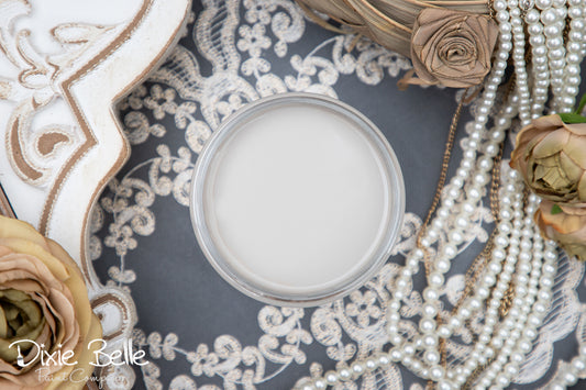 Close-up of a french linen paint jar with pearls and flowers on a textured surface, featuring the brand 'Dixie Belle'.
