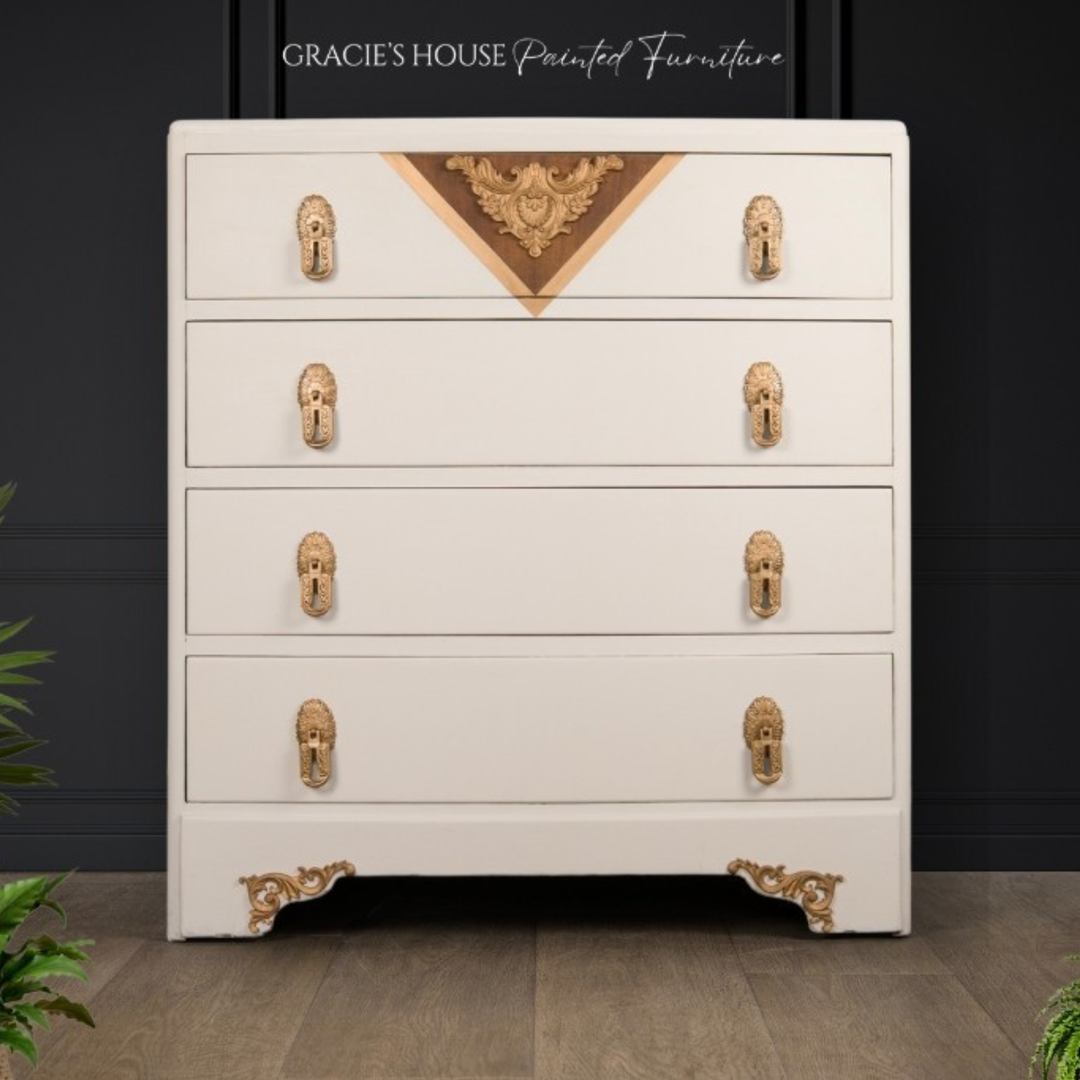 A white five-drawer chest of drawers with ornate gold handles and decorative gold corner accents, set against a dark paneled wall with a wood floor. The text 'GRACIE'S HOUSE Painted Furniture' is visible at the top.