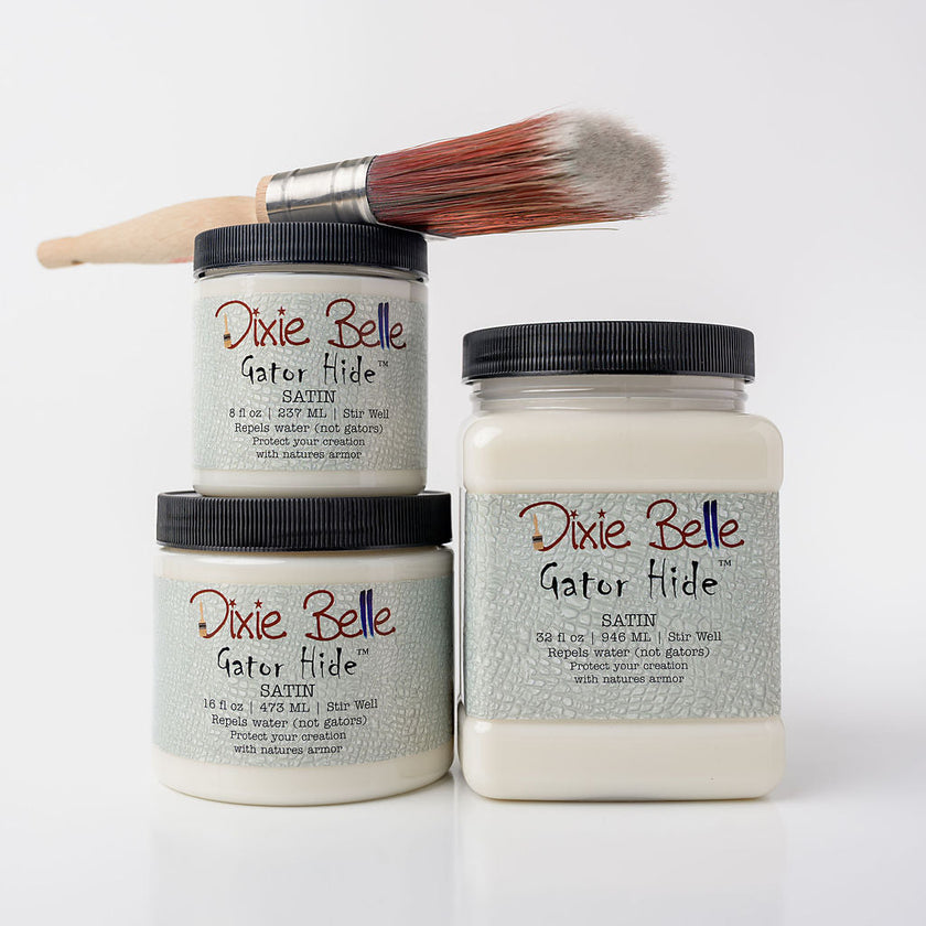 Three jars of Dixie Belle Gator Hide clear coat with a paintbrush resting across the top jar, set against a clean white background.