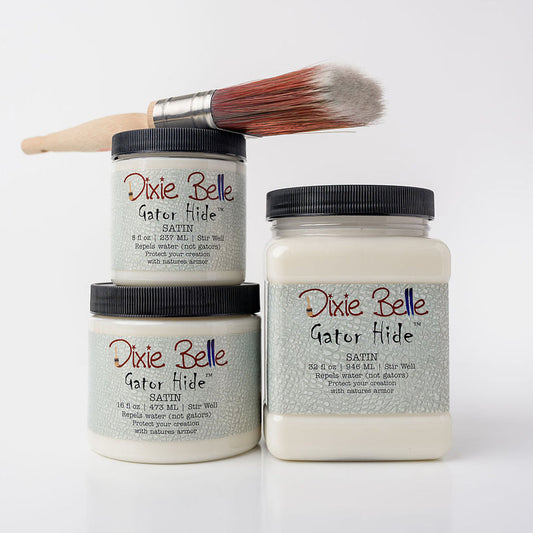 Three jars of Dixie Belle Gator Hide clear coat with a paintbrush resting across the top jar, set against a clean white background.
