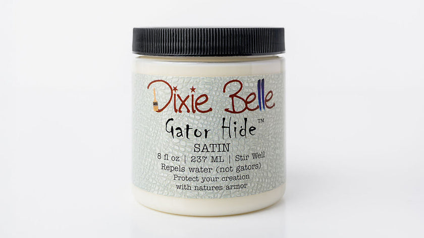 A jar of Dixie Belle Gator Hide Satin clear coat on a white background. The jar contains off-white wax and has a black screw-on lid with a textured light gray label.