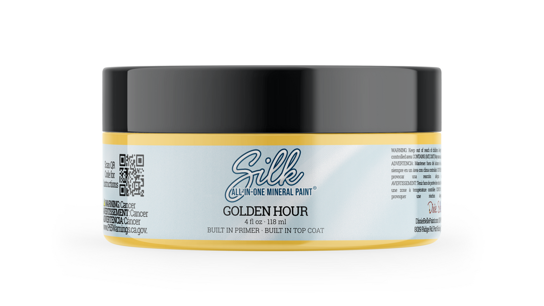 A jar of Silk All-In-One Mineral Paint in the Golden Hour shade, featuring a black lid, a white label with gold accents, and a yellow-gold base, shown on a clean white background.