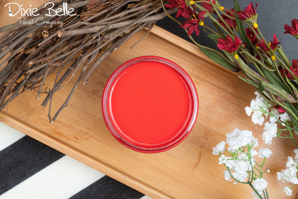 A jar of Honky Tonk Red paint, placed on a wooden tray with decorative twigs, red flowers, and white baby's breath. The Dixie Belle Company logo appears in the top left corner.
