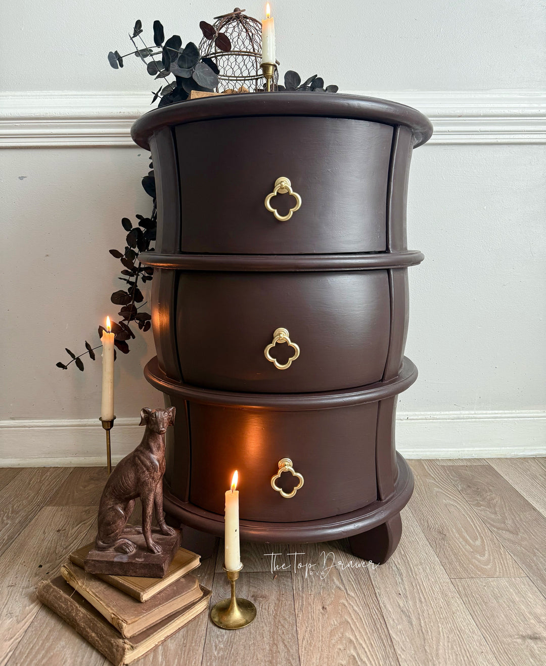 Wooden side table with three drawers, candles, and decorative items on a wooden floor.